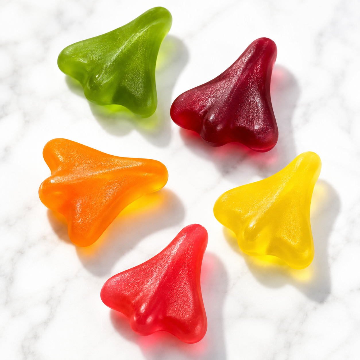 Five translucent gummy shark-tooth candies in green, burgundy, orange, yellow, and red, arranged on a white marble surface.